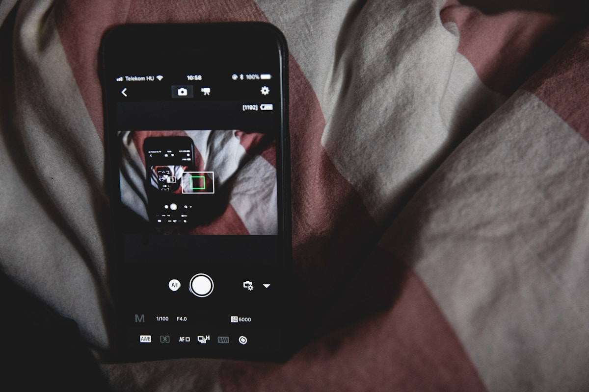 A smartphone lying face up on rumpled striped bedsheets in a dark room, its screen the only source of light